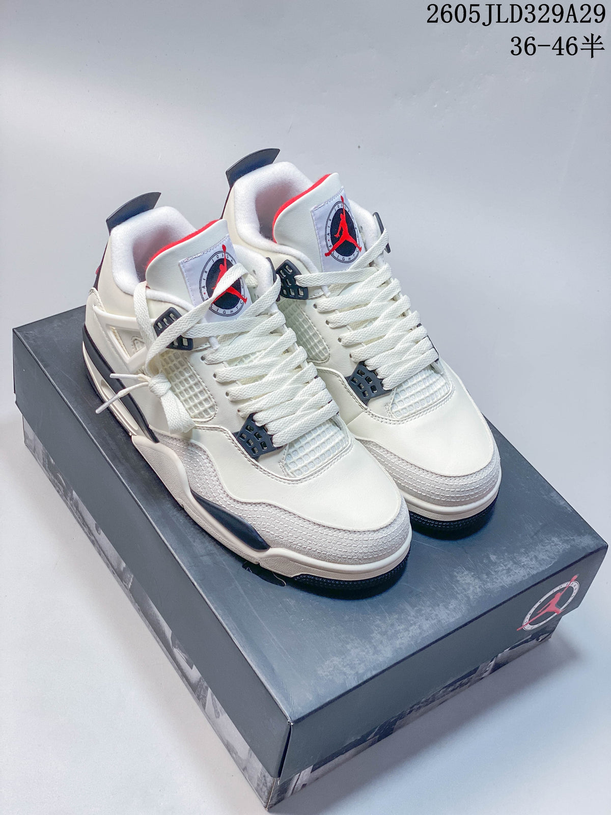 Pair of white Jordan Air Jordan 4 Retro OG mid-top sneakers with dark accents, shown on a shoe box.