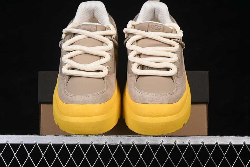Front view of the pair highlighting the taupe uppers, cream laces, and yellow soles