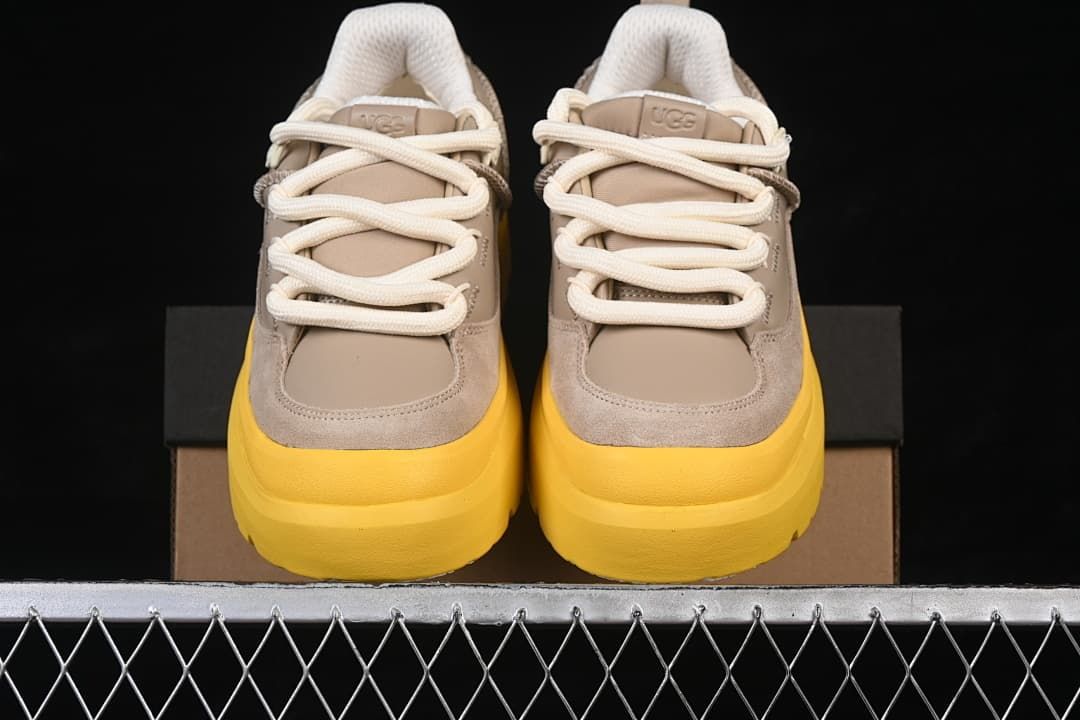 Front view of the pair highlighting the taupe uppers, cream laces, and yellow soles