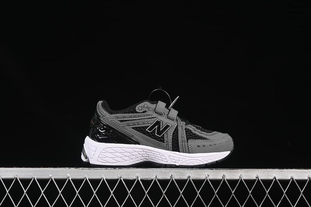 Side profile of one black and gray sneaker with a white midsole and hook-and-loop straps.