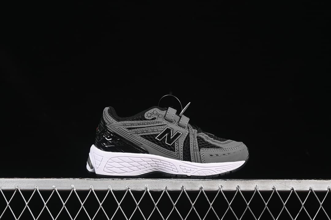 Side profile of one black and gray sneaker with a white midsole and hook-and-loop straps.