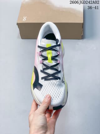 Top view of one sneaker showing the white mesh-textured upper, black laces, neon yellow tongue detail, and pink side accents.