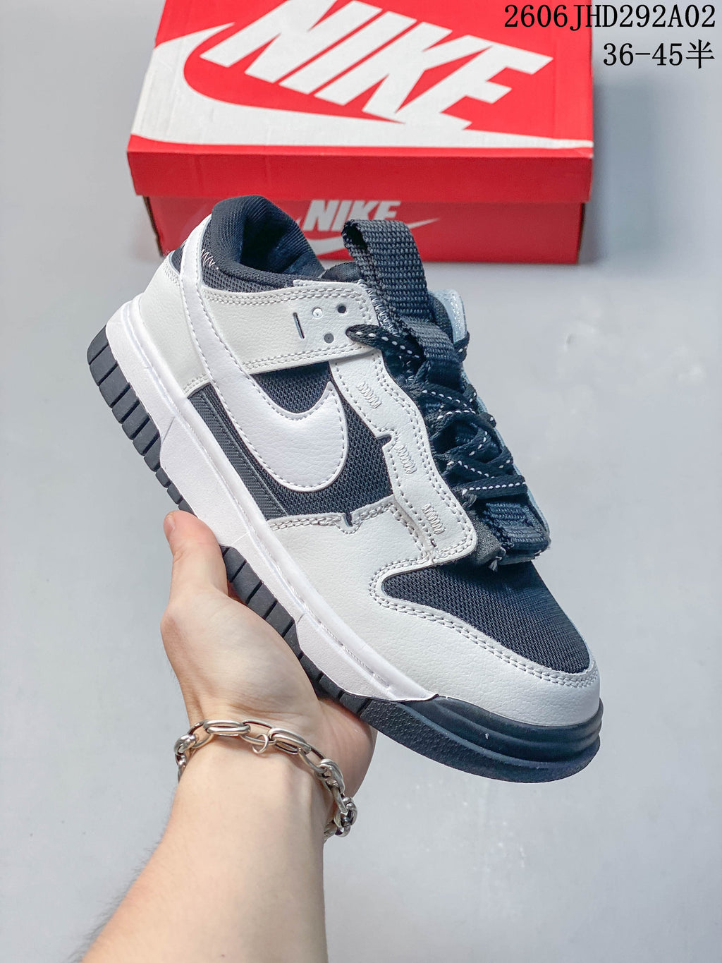 White and navy Nike SB Dunk low-top sneaker with a dark outsole, shown beside a Nike shoe box.