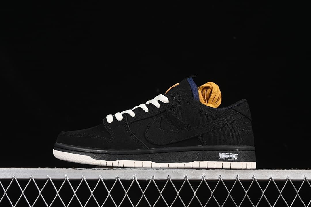 Side profile of a black low-top Nike SB Dunk with off-white outsole, white laces, and golden-yellow spare laces