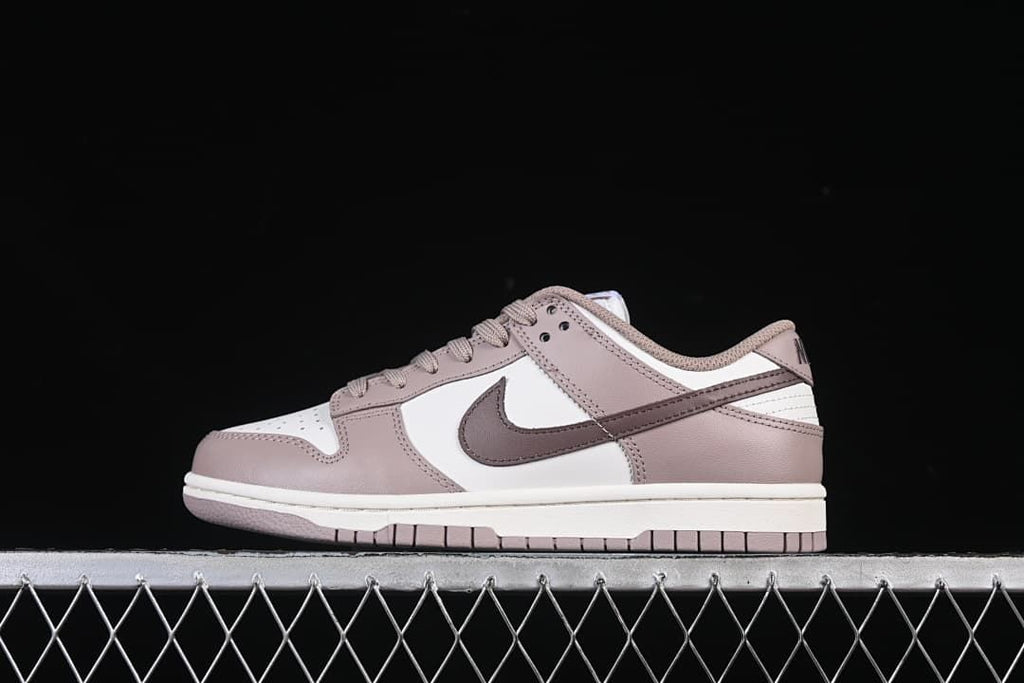 Side profile of a pink and white low-top sneaker against a dark background.