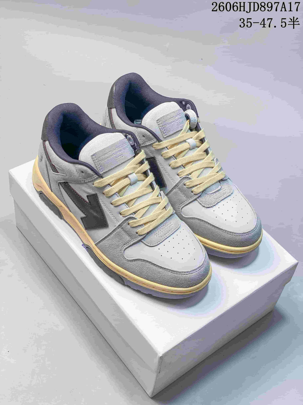 Pair of white and grey low-top sneakers with dark arrow-shaped side details and pale yellow midsole accents