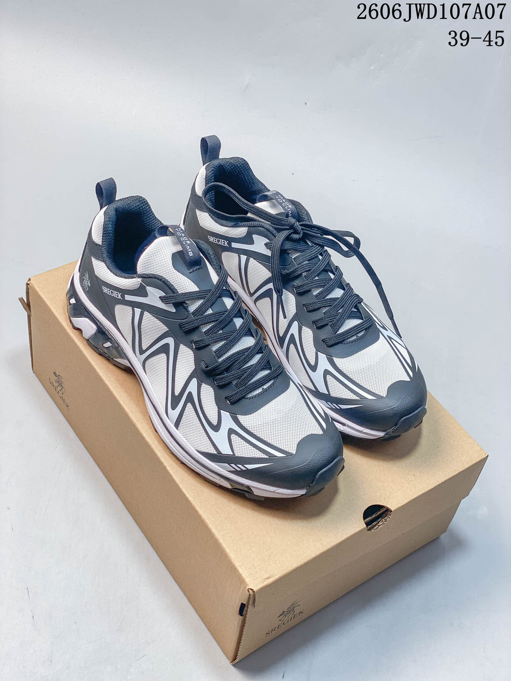Pair of gray and white Sregiek low-top hiking shoes with dark laces, shown on a shoe box; image text shows style code 2606JWD107A07 and size range 39–45.