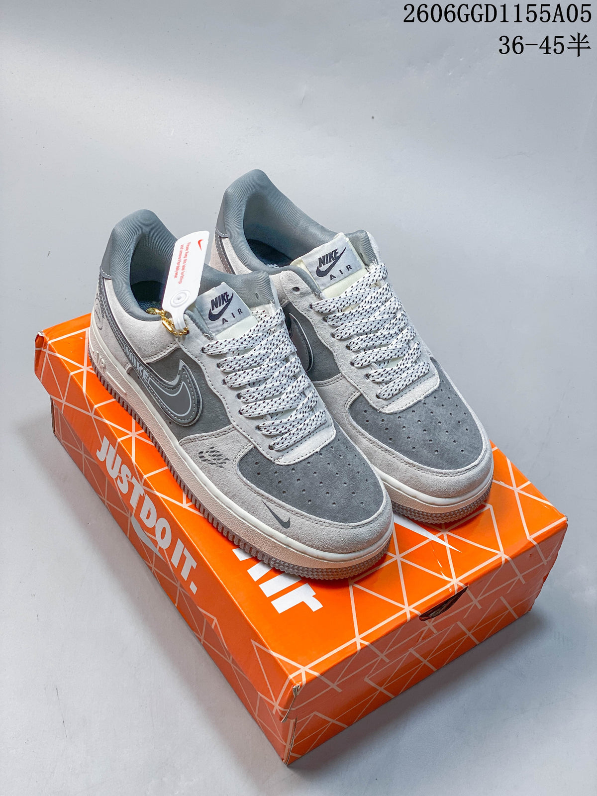 Pair of grey and white Nike Air Force 1 low-top sneakers with patterned laces and a hanging charm
