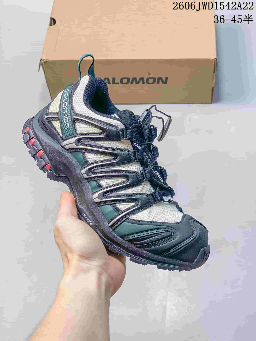 White and dark teal Salomon trail-style sneaker with red outsole accents.