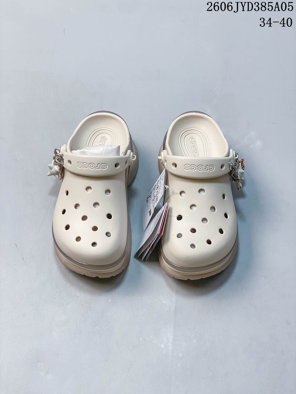 Pair of warm off-white platform clogs with decorative charms and adjustable heel straps.