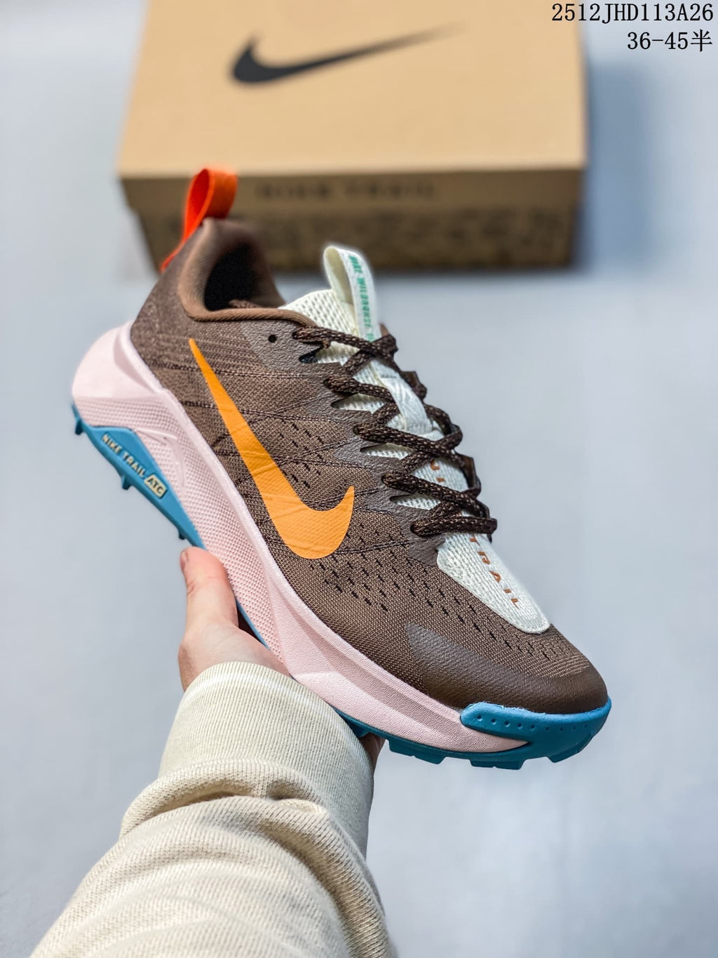 Angled side view of a Nike ReactX Wildhorse 10 with an orange swoosh, brown upper, pale pink midsole, and blue outsole.
