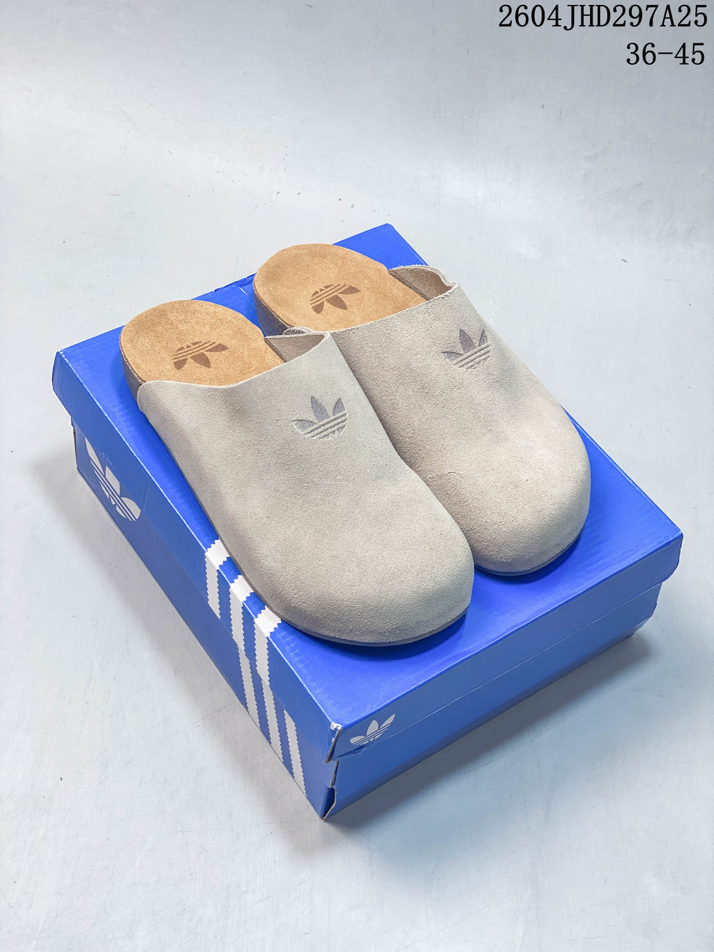 Pair of light beige Adidas Adimule closed-toe mules on a blue box