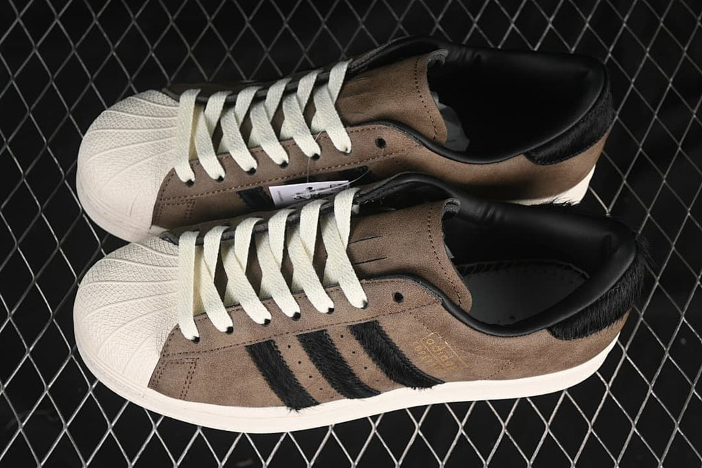 Pair of brown and black Superstar sneakers with off-white shell toes and laces