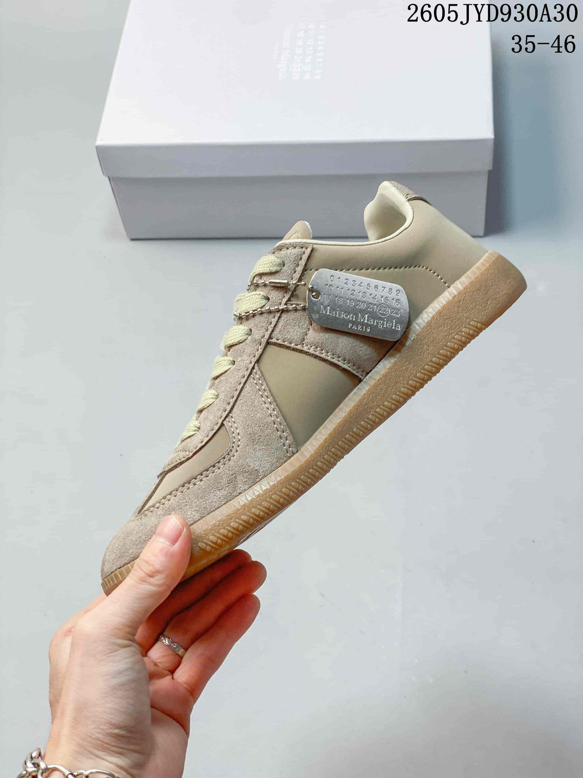 Side profile of a taupe low-top sneaker with contrast panels and a small metal tag.