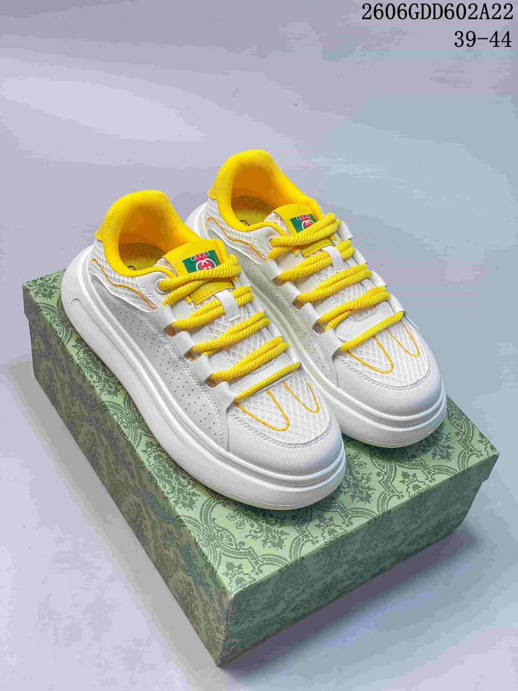White and yellow low-top sneakers displayed on a green patterned box