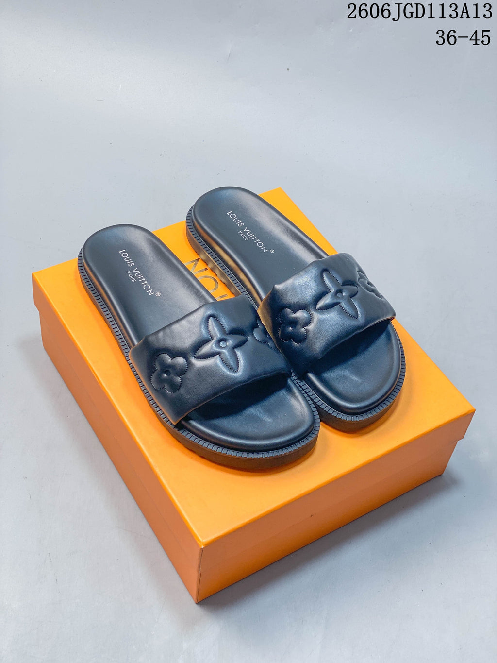 Dark slide sandals with raised floral motifs and a thick ridged outsole, photographed on an orange box.