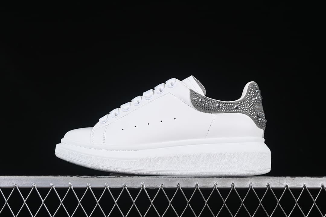 Side view of a white low-top sneaker with a crystal-embellished silver-tone heel tab.