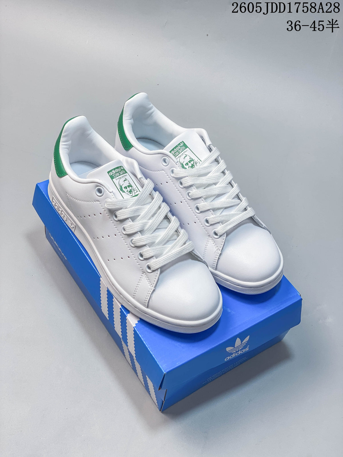 Pair of white Adidas Stan Smith sneakers with green heel tabs on a blue shoe box