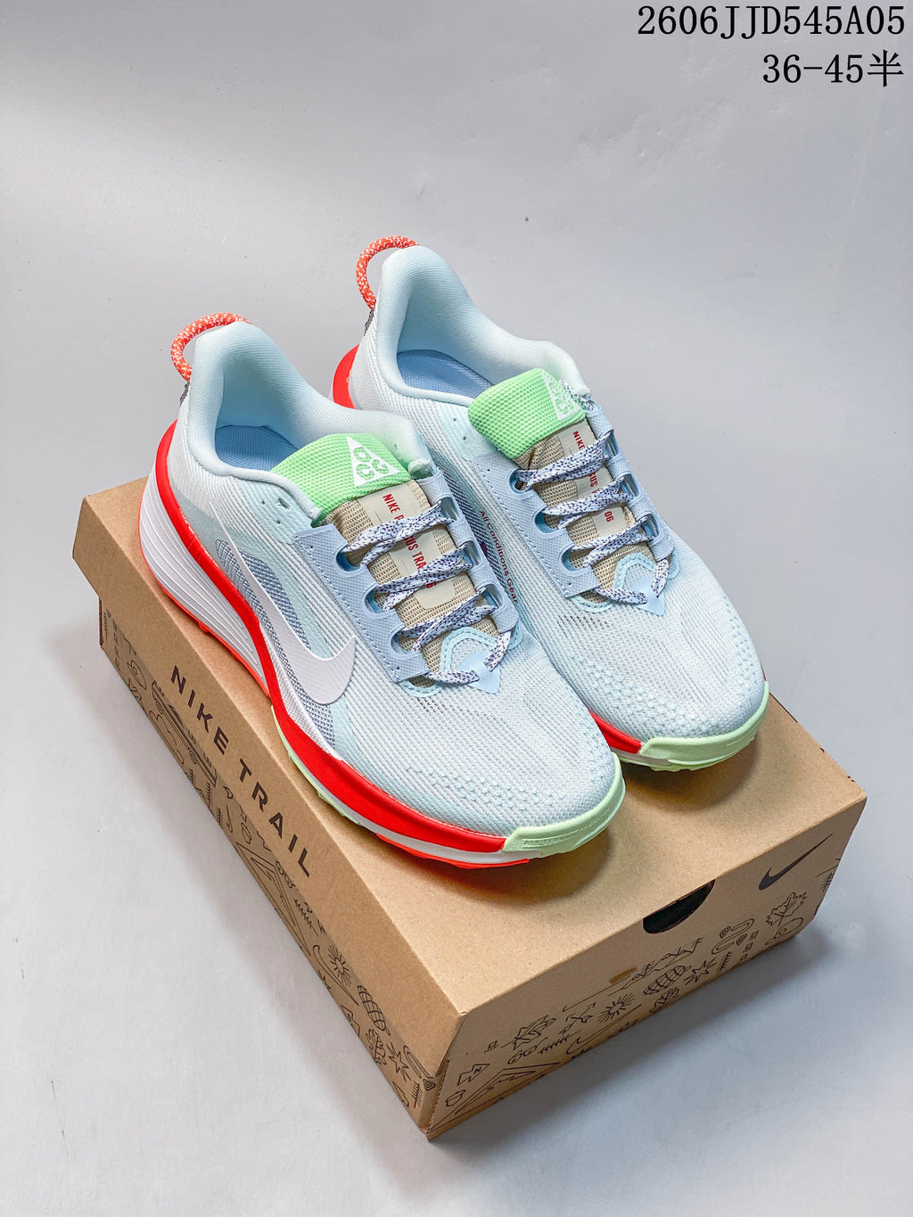 Pair of light blue Nike Pegasus Trail 6 shoes on a box, showing bright red-orange and pale green accents.