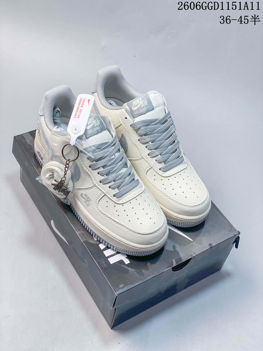 Off-white and gray low-top sneakers displayed on a shoebox with a detachable charm and spare laces
