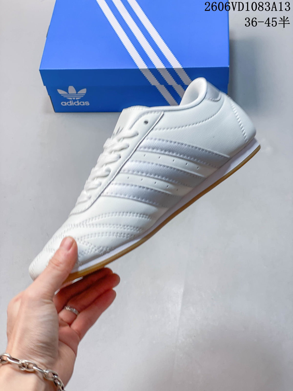 Side view of a white low-top sneaker with silver-tone stripes and a gum-colored outsole.