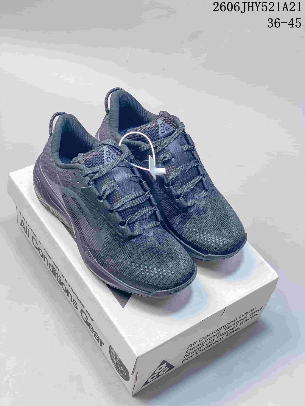 Pair of dark gray Nike ACG lace-up shoes on a box, shown from the front and side.