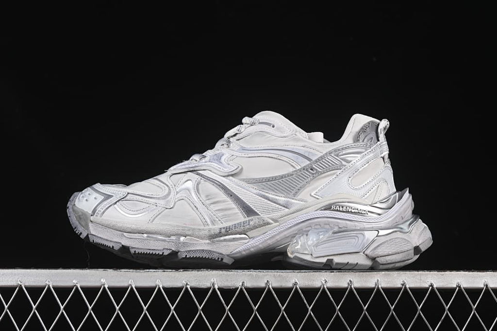 Side view of a grey and silver Balenciaga Runner 2 sneaker against a dark background.