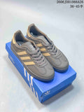 Pair of grey Adidas Gazelle Indoor sneakers with gold-tone stripes, shown on a blue shoe box
