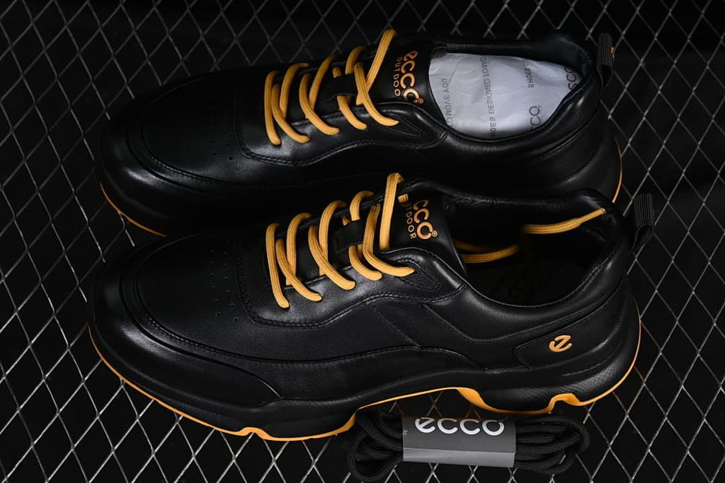 Pair of black sneakers with amber laces and a spare lace bundle