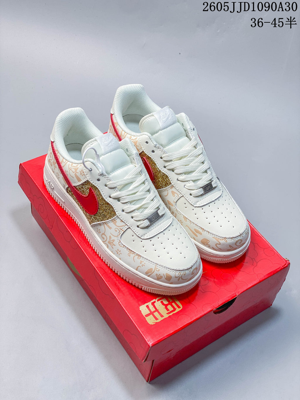 Pair of ivory low-top sneakers with tan ornamental print, glittery gold panels, red Swoosh accents, and a red box