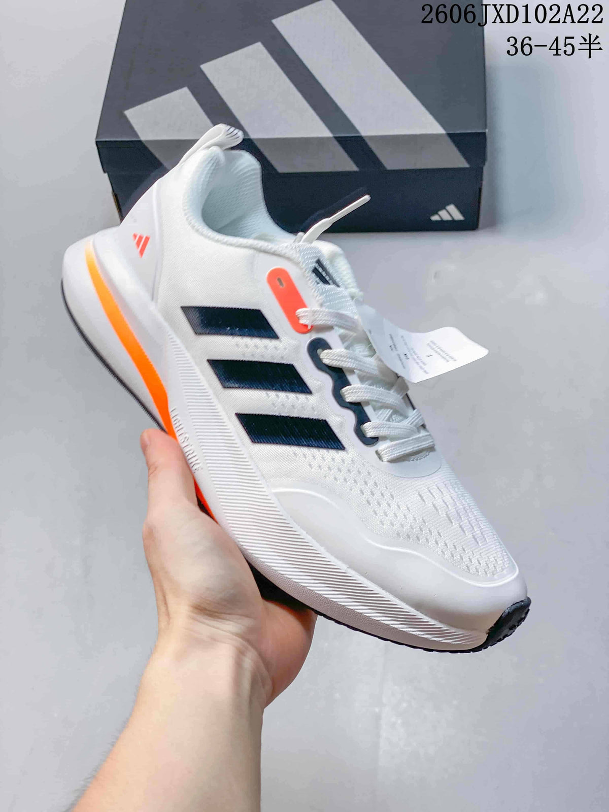Side view of a white Adidas sneaker with dark stripes and orange accents.