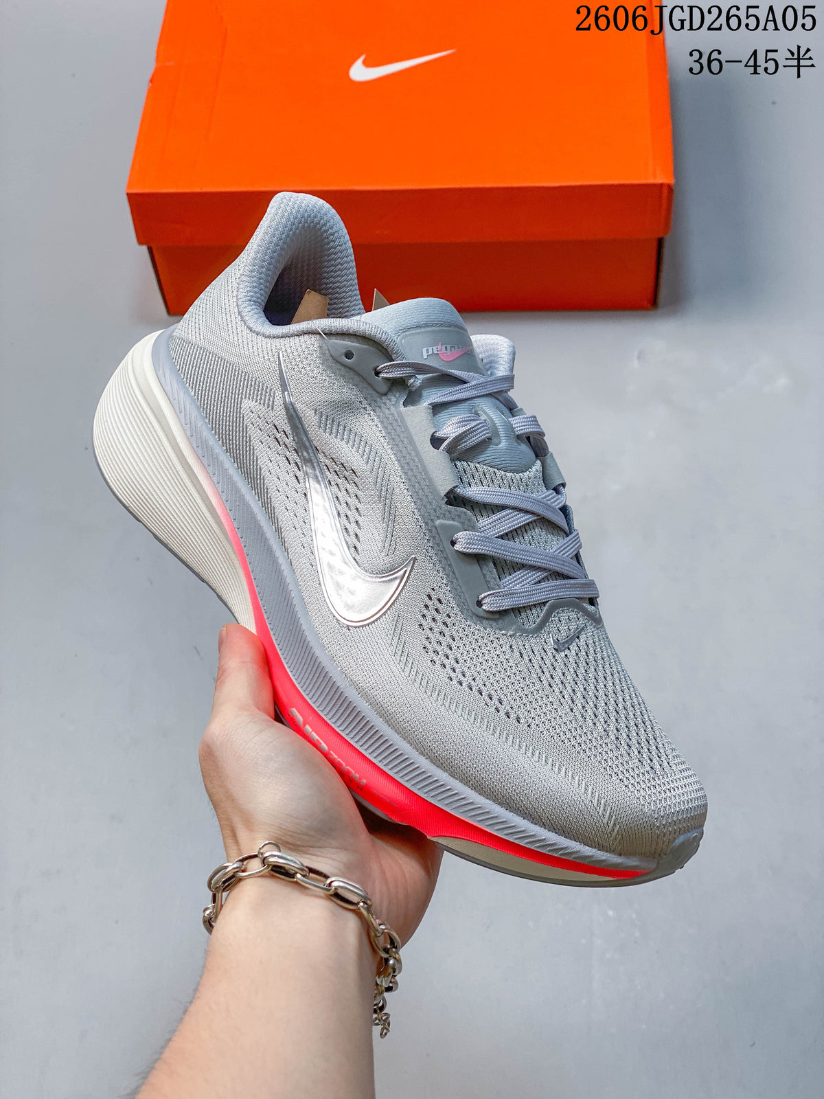Light gray Nike Pegasus 42 running shoe with coral accents, shown beside an orange shoebox.
