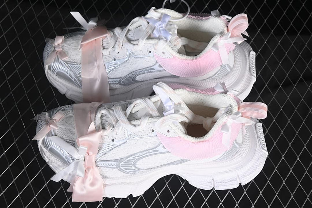 Pair of white sneakers with silver-toned details, pink collar trim, and ribbons.