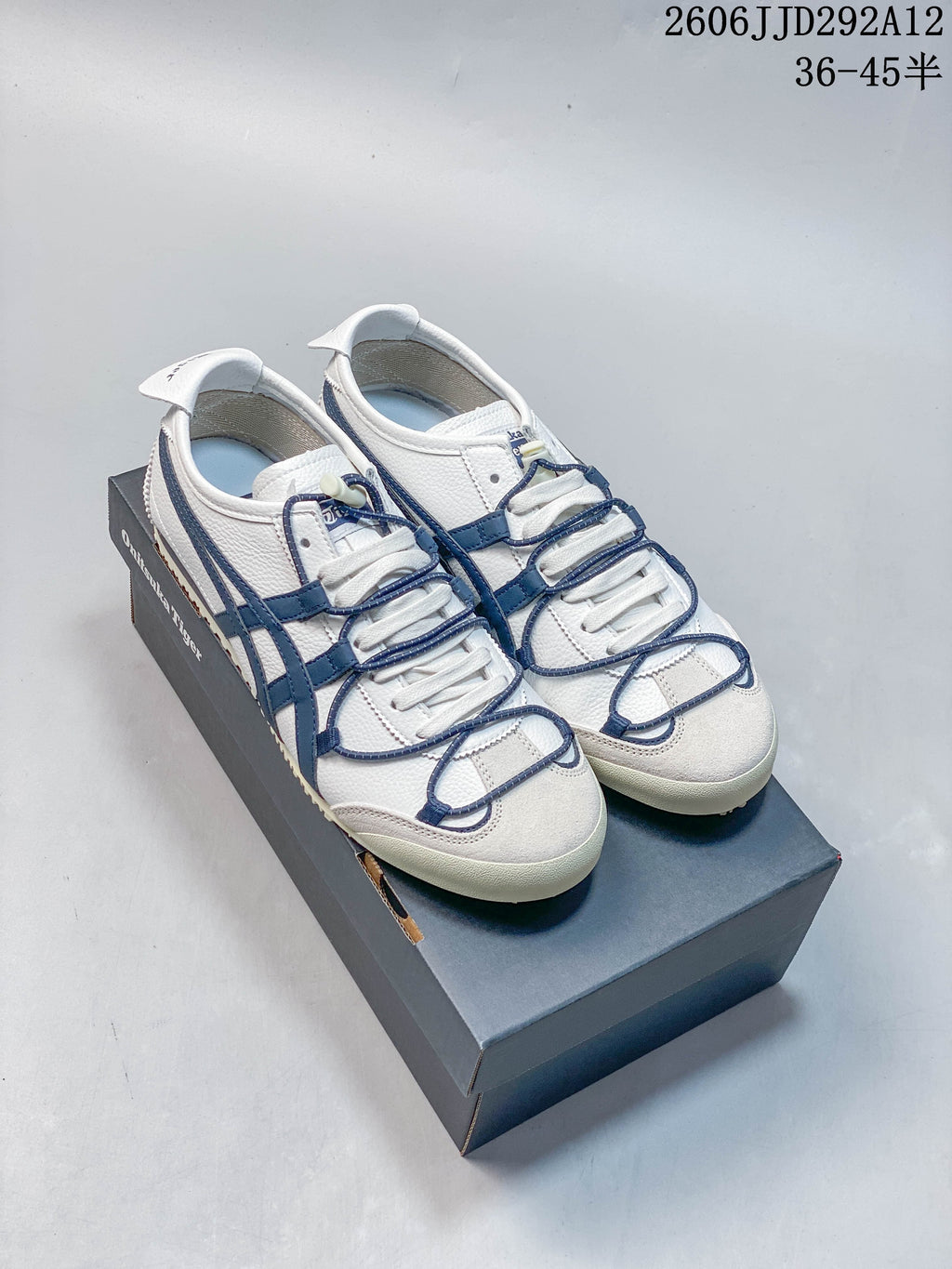 White Onitsuka Tiger Mexico 66 Deluxe sneakers with blue accents, photographed on a shoe box.