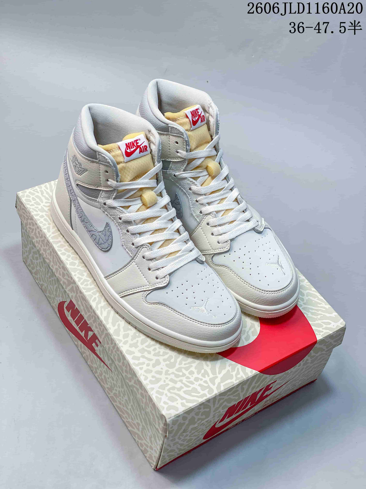 Pair of white and grey Air Jordan 1 high-top sneakers displayed on a patterned box