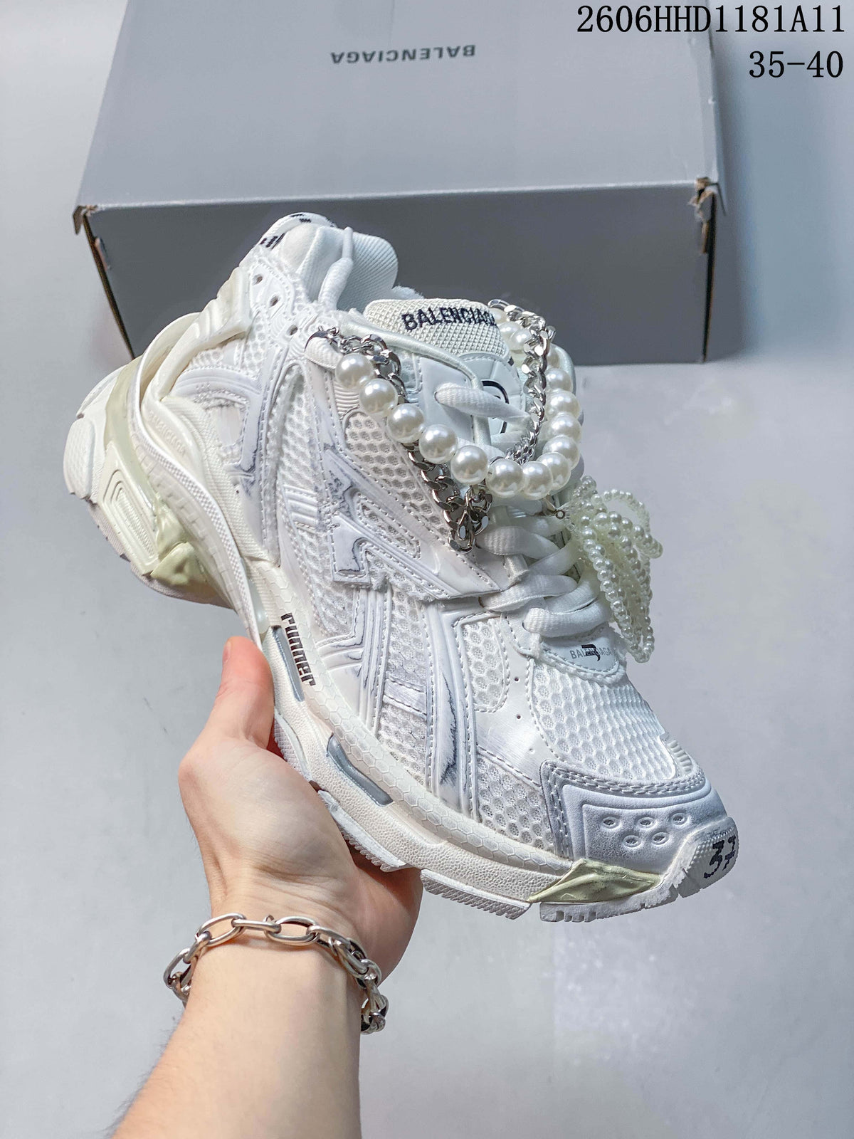 Angled side view of the white sneaker highlighting its textured panels and decorative lace accessories.