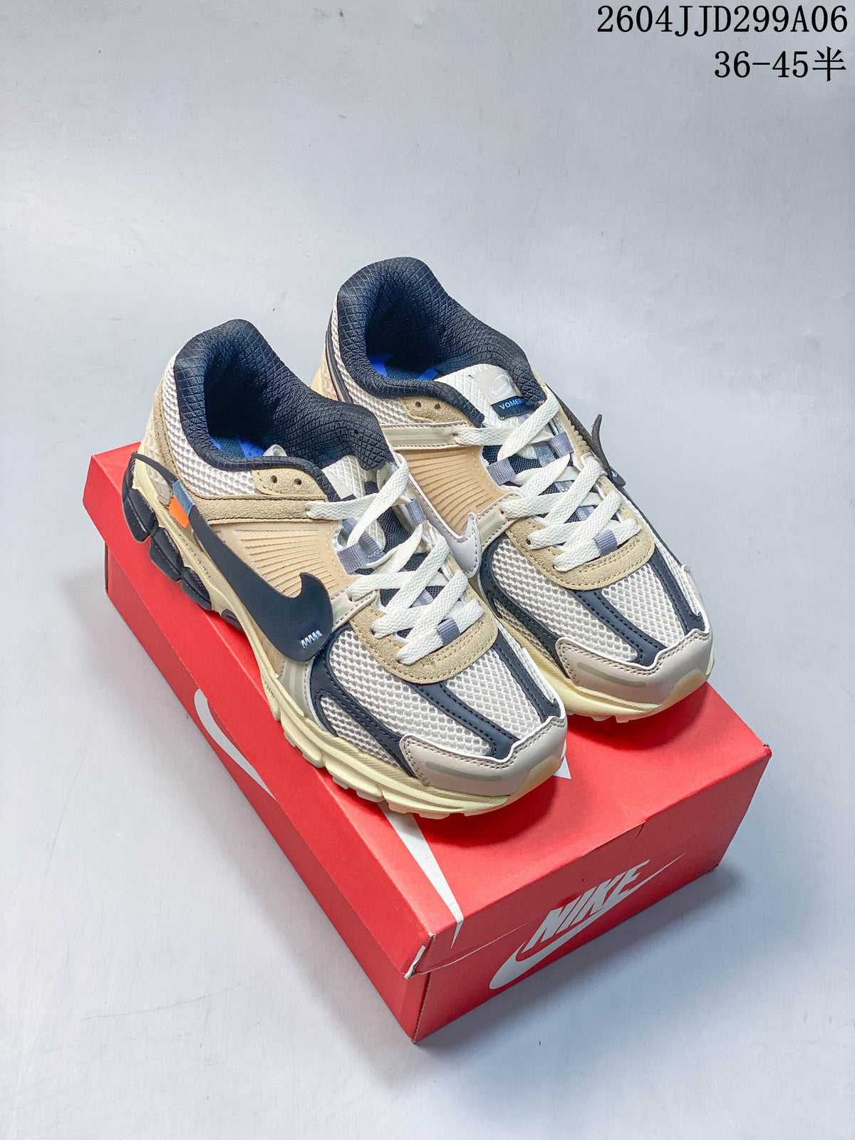 Pair of beige and cream Nike Zoom Vomero 5 sneakers with dark gray accents on a red shoe box.