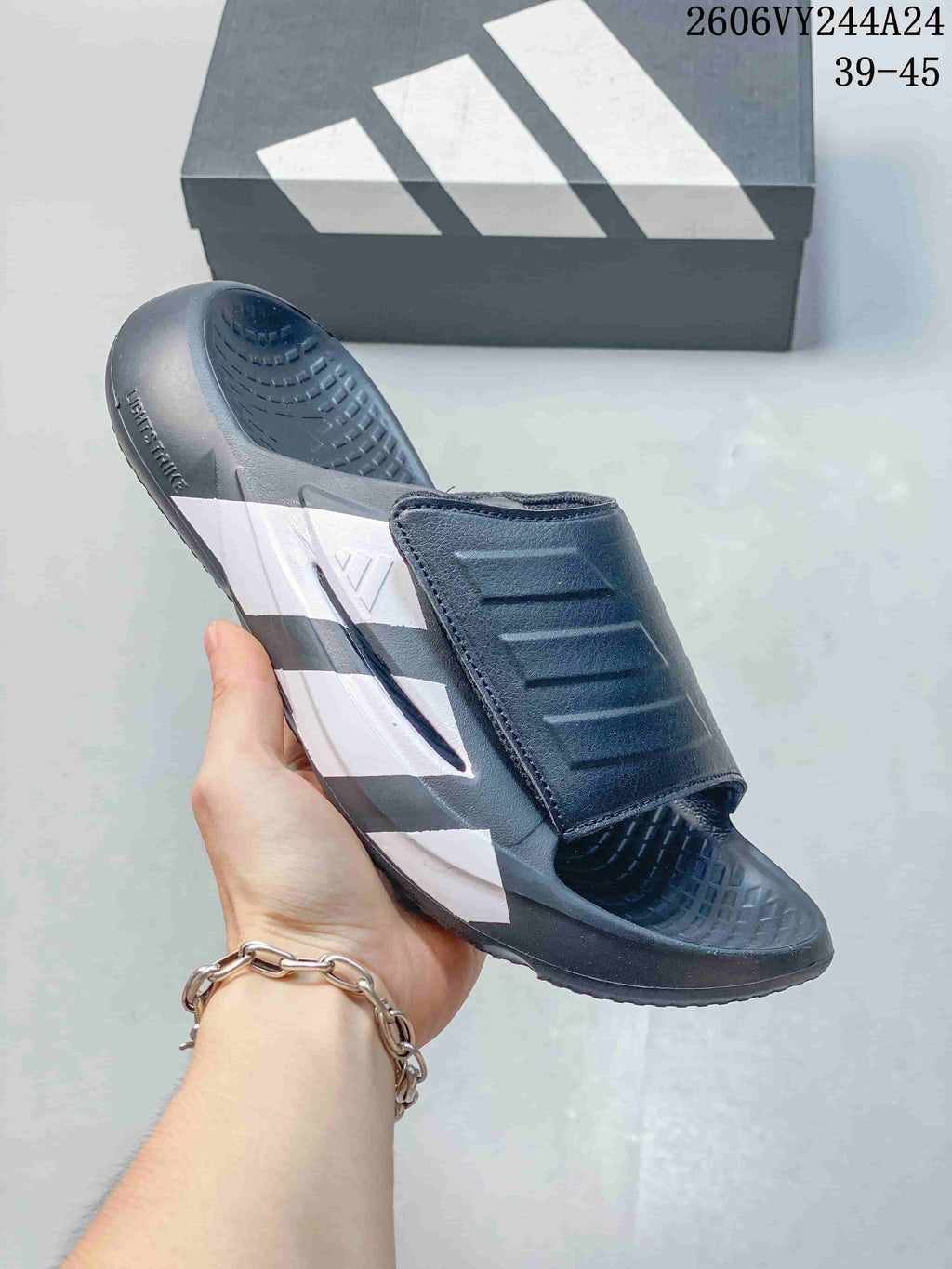 Dark gray adidas Lightblaze slide with white stripe detailing, shown beside a box; image overlay lists sizes 39–45.