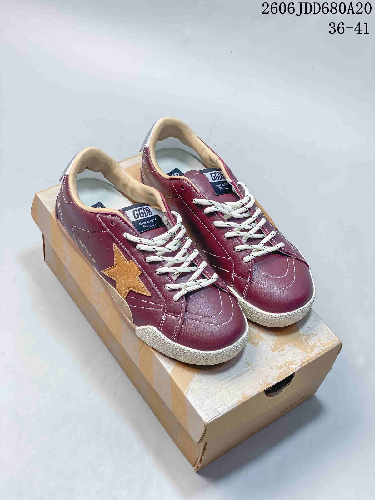 Pair of burgundy Golden Goose Super-Star low-top sneakers with tan stars and white laces, displayed on a shoebox