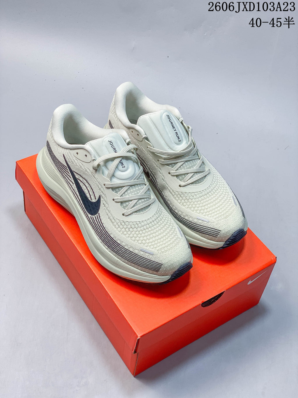 Light neutral Nike running shoes with dark accents, shown on an orange shoe box.