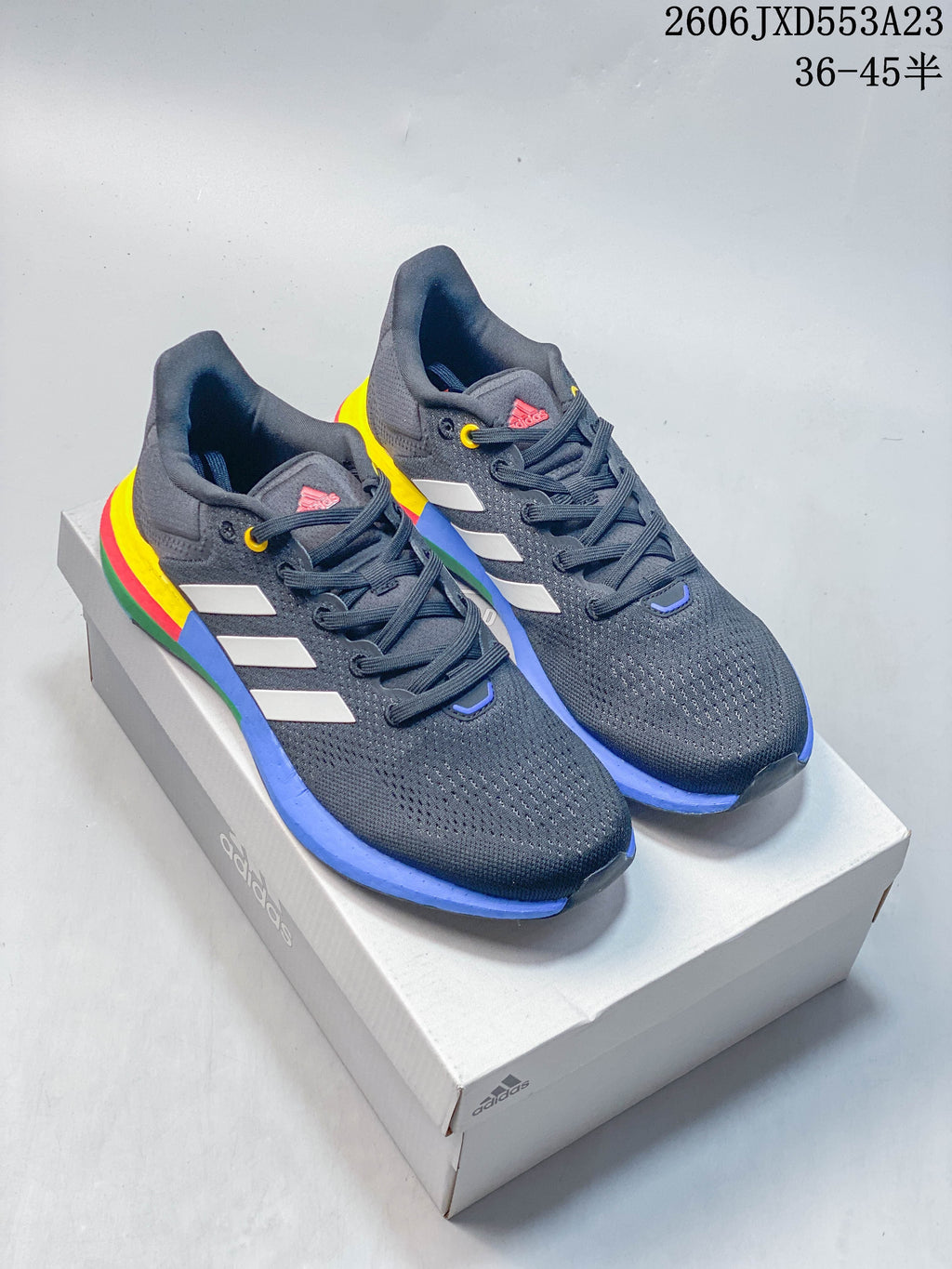 Pair of charcoal Adidas PureBoost 21 shoes with white stripes and a colorful sole, displayed on a shoebox