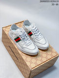 Pair of white low-top sneakers with green-and-red side stripes displayed on a patterned shoe box.