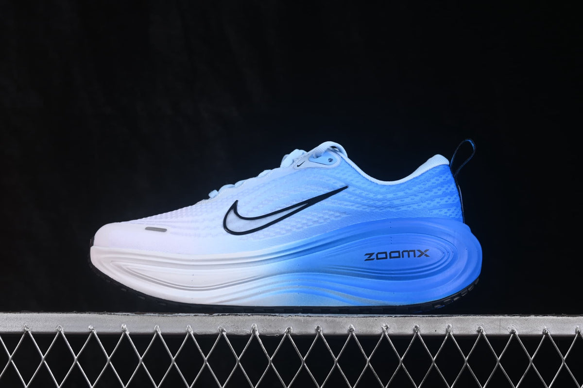 Side view of white and blue Nike Air Zoom Vomero Plus running shoes with black Swoosh branding and a sculpted blue midsole.