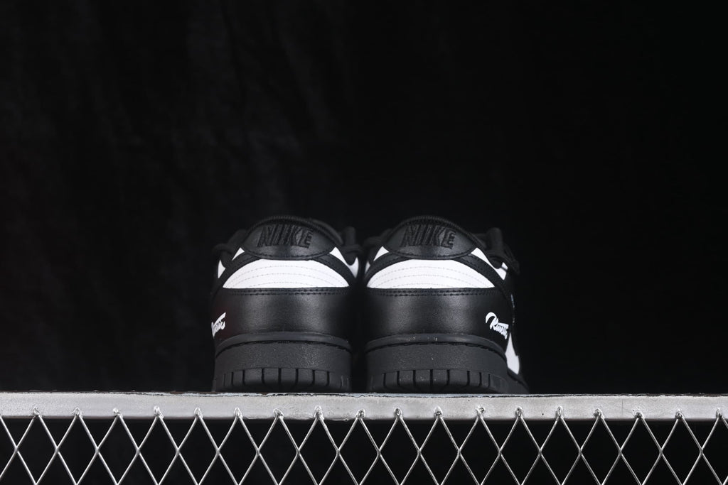 Rear view of black and white Nike SB Dunk Low sneakers showing black heels, white collar panels, and black outsoles.
