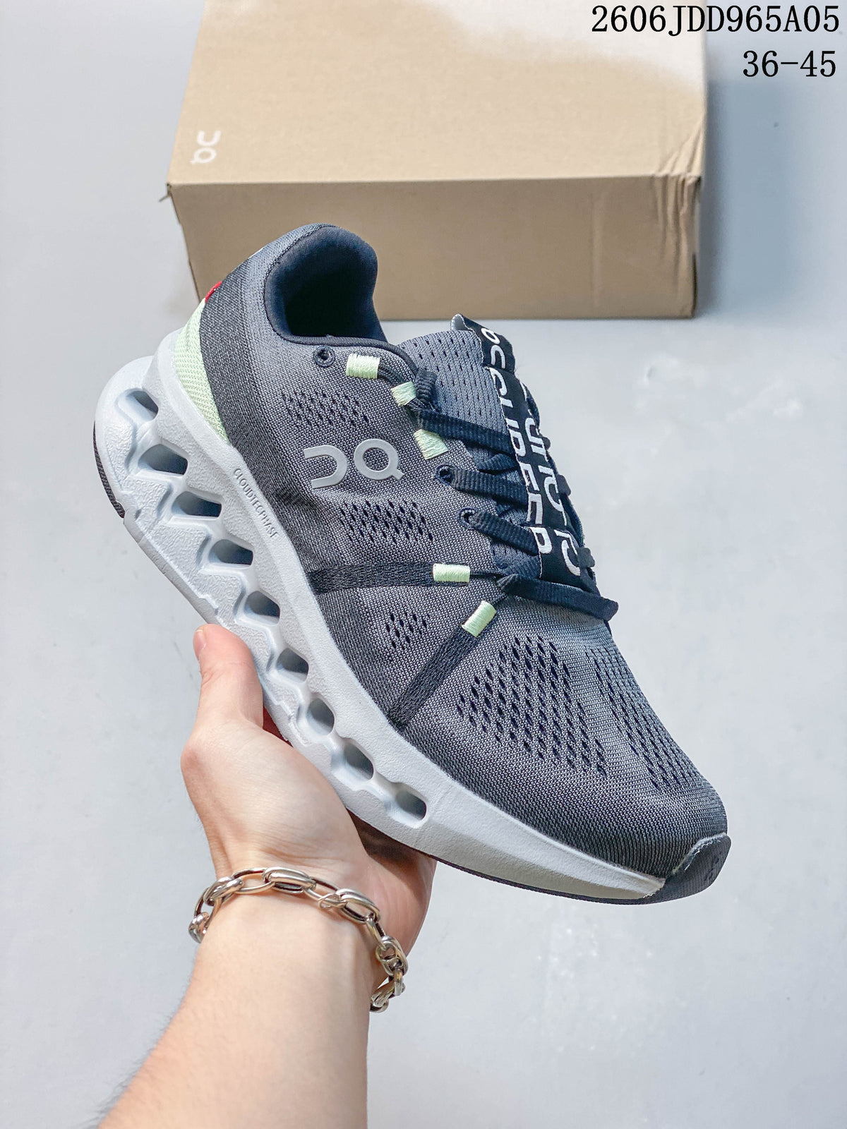 Dark gray On Cloudsurfer Trail shoe with a white sculpted sole and pale green accents