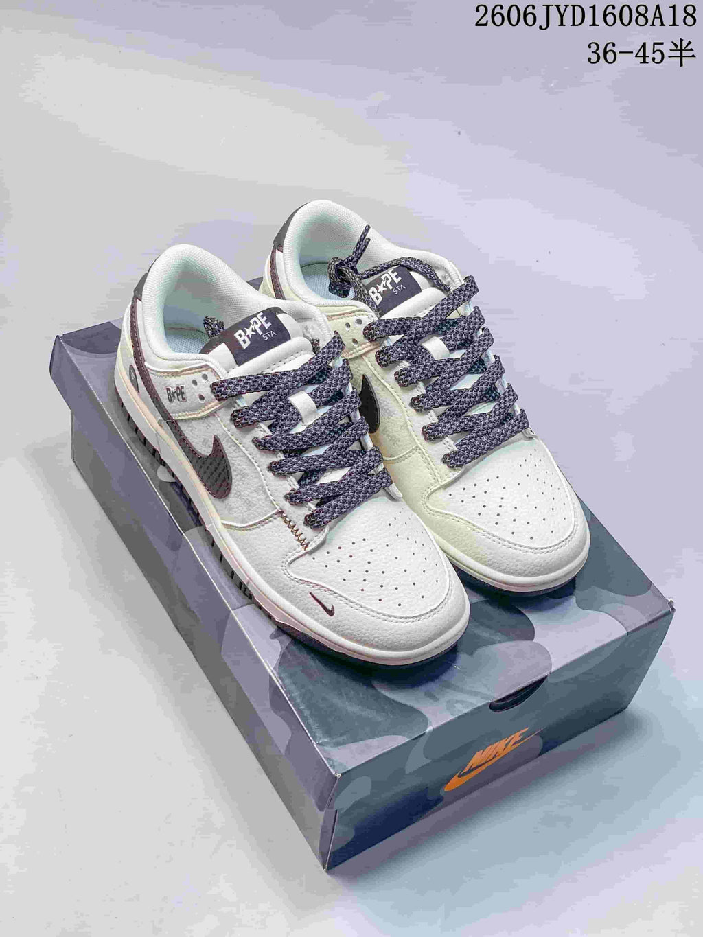 Pair of cream and grey low-top sneakers with dark patterned laces on a camouflage-patterned box