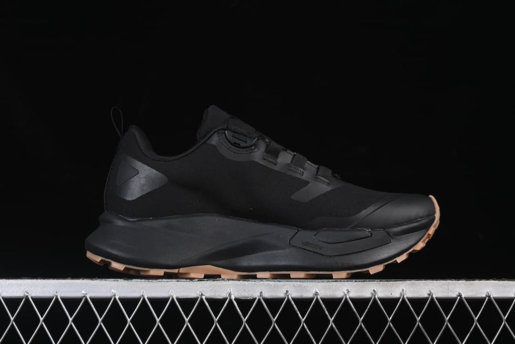 Side profile of a black low-cut trail shoe with sculpted midsole and tan-toned outsole.