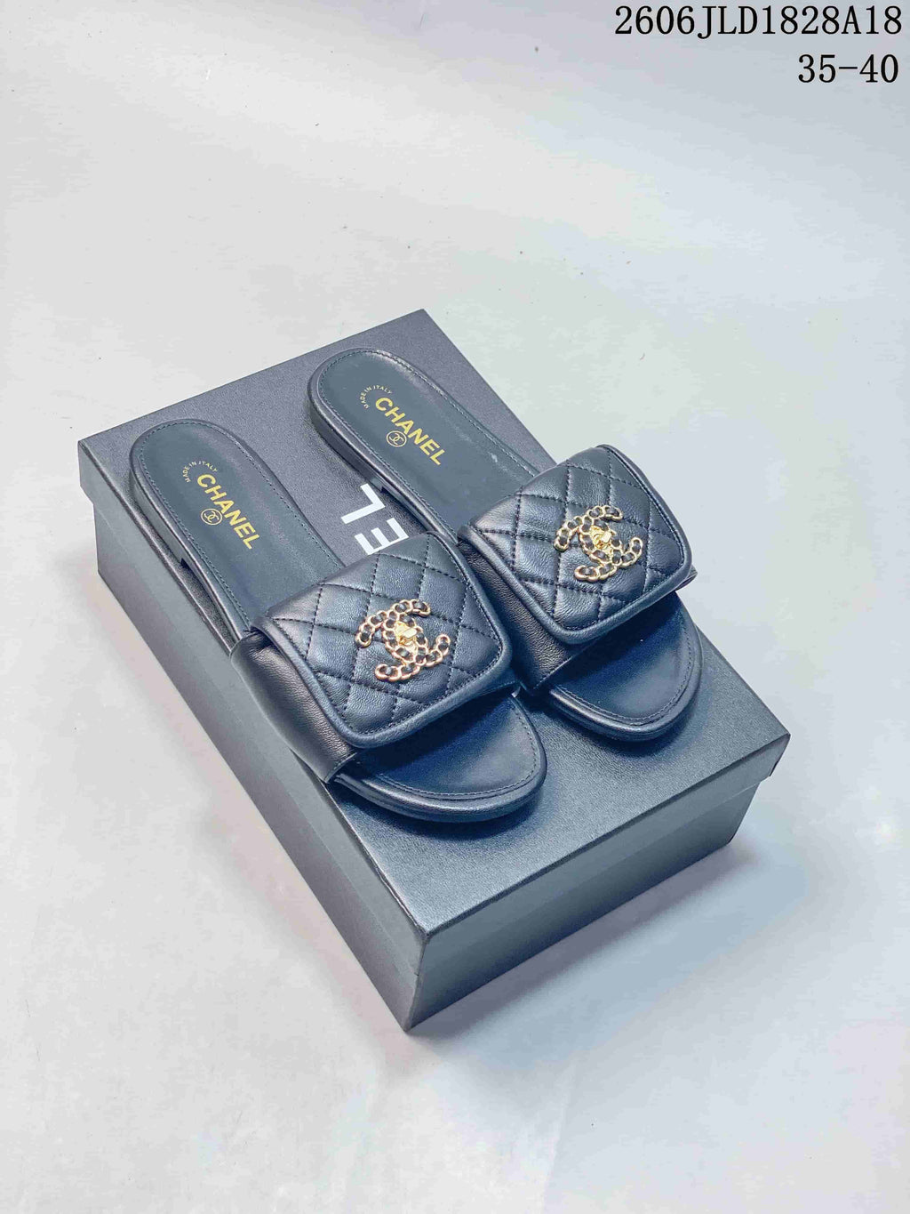 Pair of navy quilted slide sandals with gold-tone ornaments, shown on a box