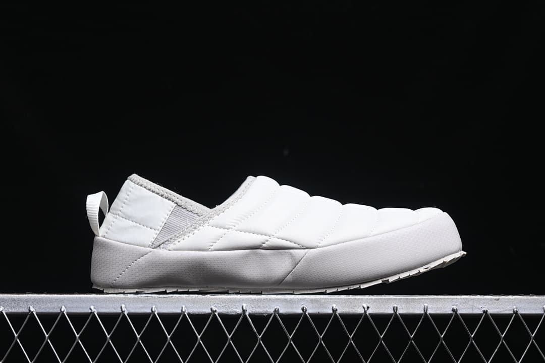 Side profile of a white quilted mule slipper.