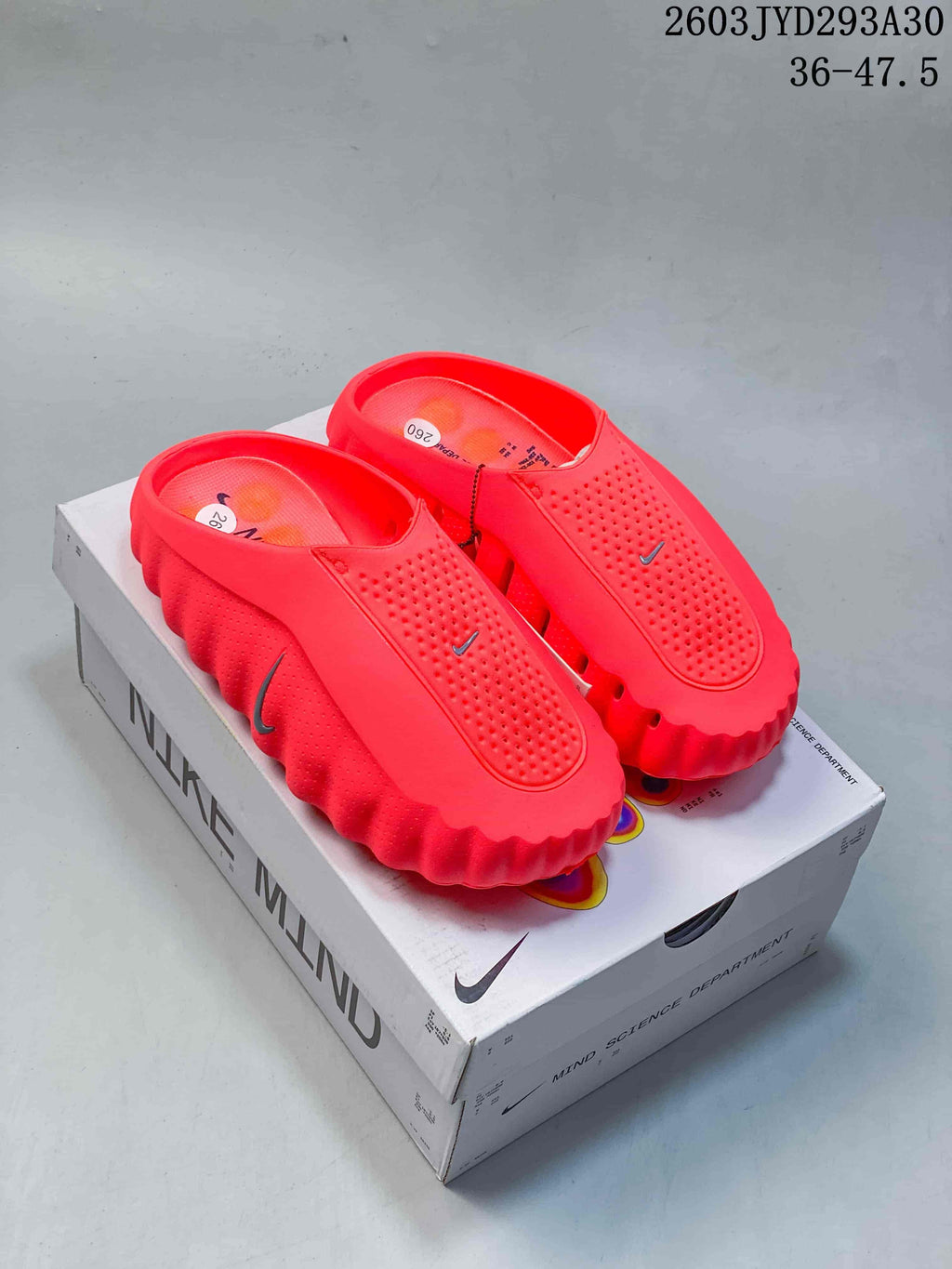 Pair of bright red Nike Mind slides with closed toes and sculpted soles, displayed on a Nike Mind box.